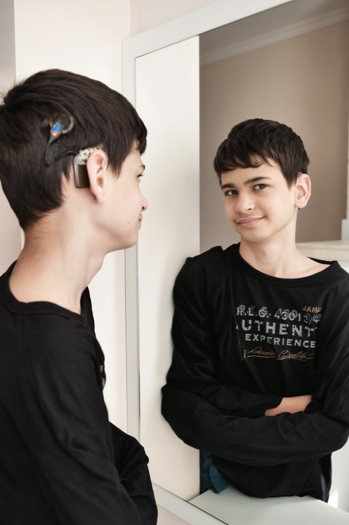 reflection in the mirror of a deaf teenage boy with a cochlear implant