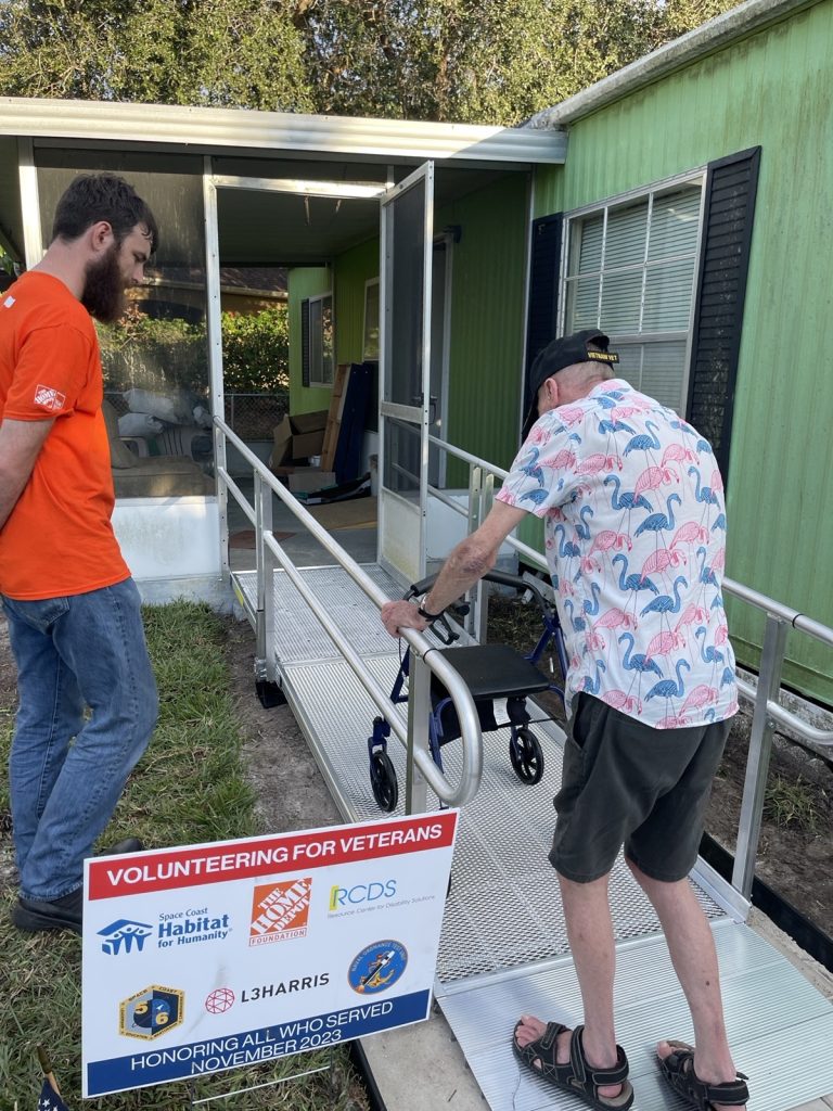 Home Depot team watching veteran use new accessible ramp outside his home. 